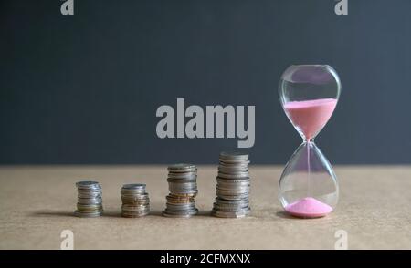 HourGlass avec sable qui coule et des pièces empilées sur la table. Le temps, c'est de l'argent. Banque D'Images