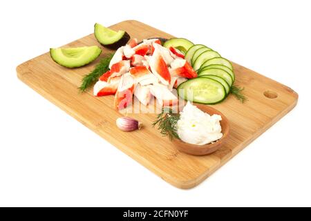 Bâtonnets de crabe viande coupée et légumes avocat coupé concombres planche à découper en bois isolée sur fond blanc Banque D'Images