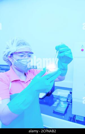 Une chercheuse asiatique portant un masque chirurgical tenant une fiole jaugée ou une éprouvette faisant des recherches en laboratoire. Mise au point douce sur la fl. Volumétrique Banque D'Images