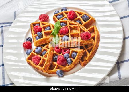 gaufres aux flocons d'avoine à la banane servies avec baies et miel sur une assiette blanche sur une table en bois avec baies, en gros plan Banque D'Images