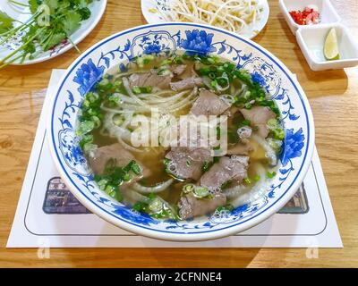 Pho Bo, une soupe vietnamienne composée de bouillon, de nouilles de riz, d'herbes et de bœuf. Cuisine populaire de rue au Vietnam. Ajout de sauce variable. Banque D'Images