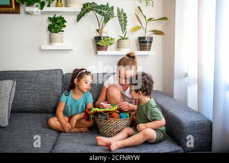 Les enfants trient ensemble, assis sur un canapé dans la maison, salon confortable. Intérieur de l'appartement avec plantes de maison. Banque D'Images