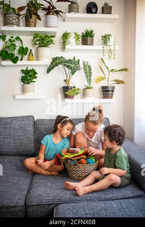 Les enfants apprennent à tricoter, assis sur un canapé à la maison. Intérieur d'appartement confortable avec plantes de maison. Banque D'Images