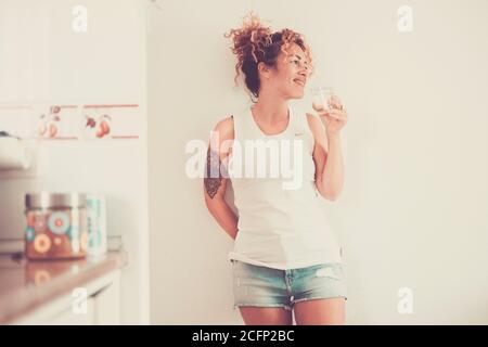 Belle jeune femme d'âge moyen caucasienne debout à la maison et boire de l'eau saine - jolie femme avec fond blanc souriant - modèle tatooté p Banque D'Images