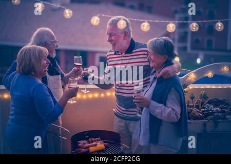 Groupe d'amis âgés joyeux et heureux, les gens se clinking et savourez le dîner en plein air sur la terrasse à la maison avec vue sur la ville - toutes les personnes Banque D'Images