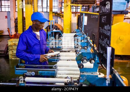 Johannesburg, Afrique du Sud - 16 octobre 2012 : ouvrier d'usine africain sur un métier à tisser de ligne de montage de trame de cobobineuse Banque D'Images