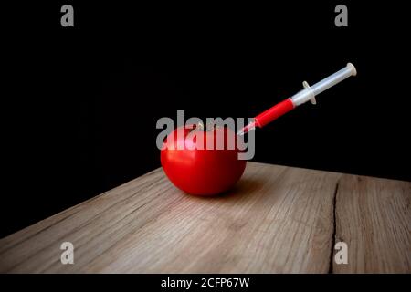 Tomate rouge mûre sur un panneau en bois et seringue à l'intérieur il extrait le liquide rouge Banque D'Images