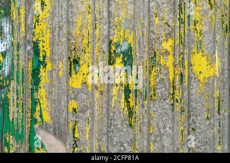 Ancienne clôture en fonte ondulée avec peinture verte et jaune qui s'écaille. Texture abstraite Banque D'Images