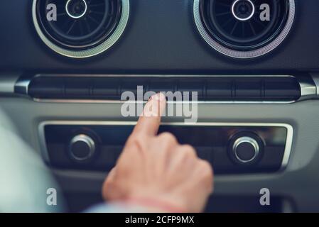 Photo courte d'une femme en appuyant sur le bouton du tableau de bord de la voiture en conduisant en ville, gros plan Banque D'Images