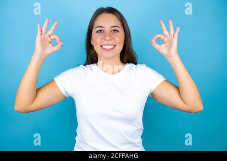 Jeune belle femme sur fond bleu isolé faisant signe ok avec les doigts et souriant, excellent symbole Banque D'Images