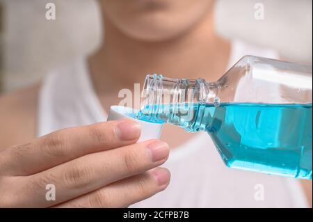 Main de l'homme versant une bouteille de rince-bouche dans le bouchon. Banque D'Images