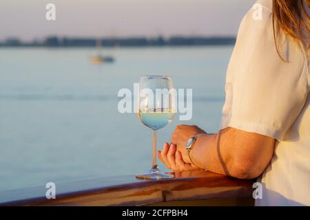 Femme de voyage de luxe buvant du vin sur un bateau de croisière au coucher du soleil Banque D'Images