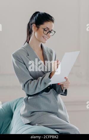 Un coup de pouce de la femme responsable vérifie le rapport financier, impliqué dans le processus de travail, signe un contrat important, a une expression heureuse, porte f Banque D'Images