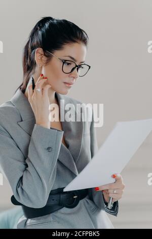 Une femme dirigeante qui a réussi examine les documents papier, analyse les données, étudie les informations de contrat, tient le stylo, porte des lunettes, ou formel Banque D'Images