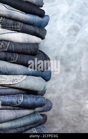 Pile de jeans pliés inlassablement sur fond gris. Gros plan de jeans de différentes couleurs. Texture ou arrière-plan denim. Copier l'espace Banque D'Images