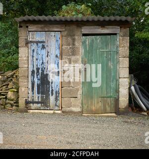 Hangar de blocs de brise avec 2 portes en bois altérées un vert et un toit en métal bleu et ondulé Banque D'Images