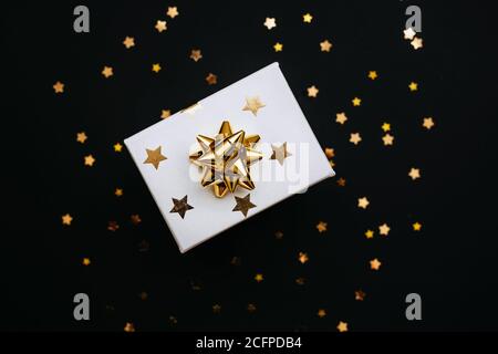 Boîte cadeau de fête avec étoiles dorées et noeud sur fond noir. Banque D'Images