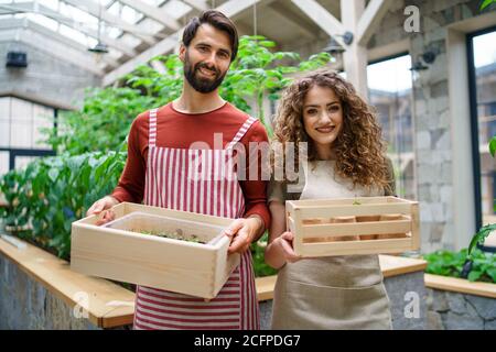 Portrait de l'homme et de la femme jardiniers debout en serre, regardant l'appareil photo. Banque D'Images