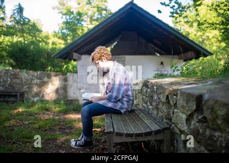 Une jeune étudiante étudie à l'extérieur seule sur un banc de parc. Plein format, lumière naturelle avec espace de copie. Banque D'Images