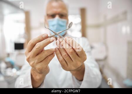 Dentiste professionnel tenant ses outils dentaires croisés Banque D'Images