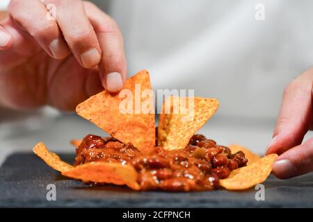 Gros plan sur les mains de sexe masculin en organisant de délicieux nachos avec du piment sur une plaque sombre Banque D'Images