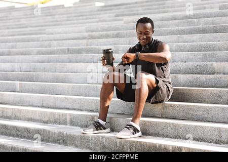 African Athete Guy Checking Fitness Tracker après l'entraînement en plein air, assis sur des marches Banque D'Images