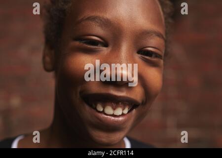 Portrait horizontal en gros plan d'un beau garçon afro-américain debout contre un mur de briques regardant l'appareil-photo sourire, espace de copie Banque D'Images