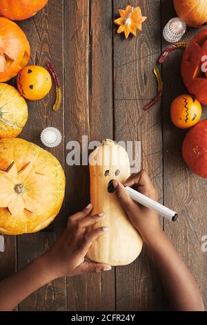 Plan vertical de haut en bas d'une personne méconnaissable dessinant un visage effrayant gourd avec marqueur arrière pour Halloween Banque D'Images