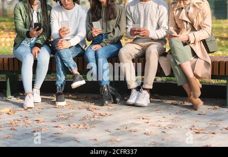 Petit groupe de jeunes amis utilisant un téléphone portable, assis sur un banc Banque D'Images