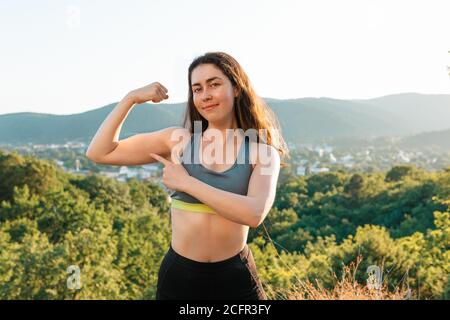 Une jeune femme sportive montre des muscles pompés du bras pendant l'entraînement dans le parc. Le concept du yoga, du sport et de la méditation. Dans la vue d'arrière-plan du Banque D'Images