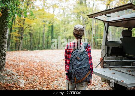 Une jeune femme caucasienne pose avec un sac à dos derrière son dos près du coffre ouvert d'une jeep. La vue de l'arrière. En arrière-plan, arbres et avant Banque D'Images