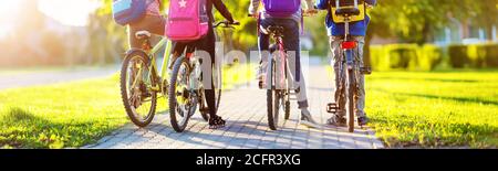 Les enfants avec des sacs à dos équitation sur des vélos dans le parc près de l'école Banque D'Images