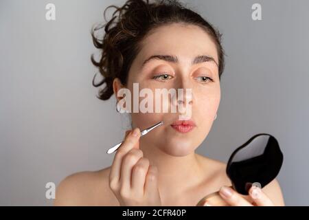 Une jeune femme regarde dans un miroir compact et tire ses antennes avec des pinces. Le concept de se débarrasser des cheveux indésirables. Banque D'Images