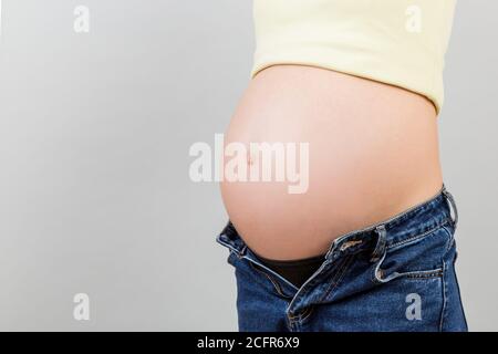 Image rognée de femme enceinte dans un Jean dézippé montrant son bosse de bébé sur fond coloré avec espace pour les copies. En attente d'un concept de bébé. Banque D'Images