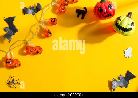 Décoration pour Halloween avec guirlande de citrouilles et de chauves-souris, chats, fantômes et jouets en plastique coupés faits à la main sur un fond jaune avec des ombres, Copy spa Banque D'Images