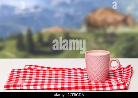 Table de petit déjeuner vide. Gros plan d'une tasse en céramique rose avec du lait sur une serviette à carreaux rouges ou une nappe sur un arrière-plan naturel flou abstrait. Templa Banque D'Images