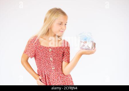 Fille blonde souriante en robe rouge montrant un cadeau Banque D'Images