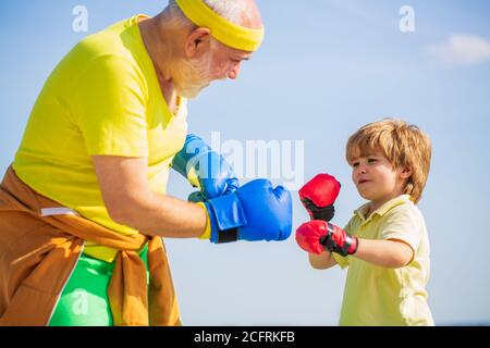 Petit garçon faisant de l'exercice de boxe avec grand-père. Le père forme sa boxe de fils. Petit sportif de garçon à l'entraînement de boxe avec entraîneur Banque D'Images