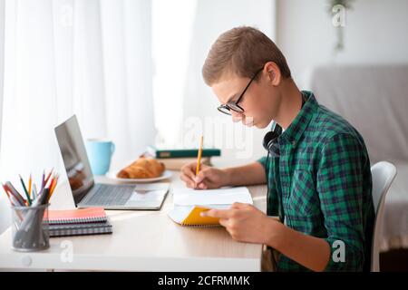 Vue latérale d'un élève intelligent qui fait ses devoirs dans la chambre Banque D'Images