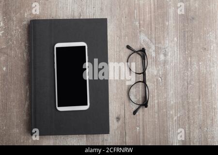 téléphone portable sur un livre noir à côté de quelques verres classiques, sur une vieille table en bois Banque D'Images