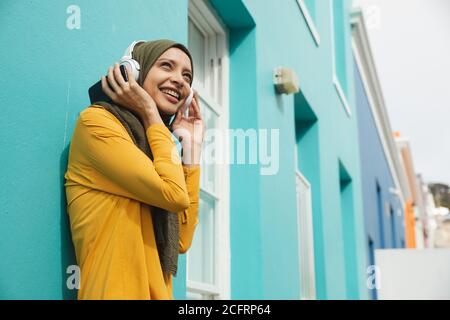 Femme en hijab écoutant de la musique avec des écouteurs à l'extérieur Banque D'Images