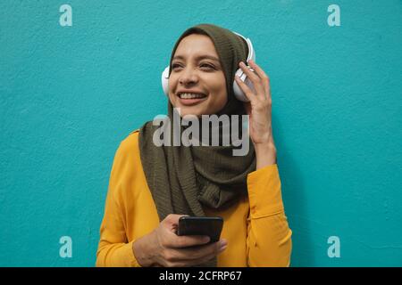 Femme en hijab portant un casque contre un mur bleu Banque D'Images