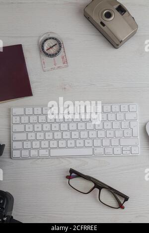 espace de travail avec clavier blanc, lunettes, ordinateur portable, boussole, ancien appareil photo. Sur un bureau en bois blanc texturé Banque D'Images