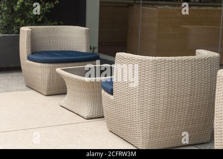 deux chaises en osier beige avec siège bleu à côté d'une petite table qui est au centre, est entouré d'un verre qui montre son reflet Banque D'Images