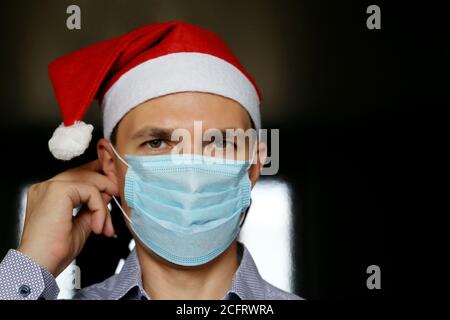 Portrait de l'homme en masque médical et chapeau du Père Noël. Célébration de Noël pendant la pandémie du coronavirus Banque D'Images