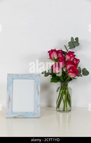 Vue d'un cadre photo, avec des roses roses placées dans un vase en verre sur fond blanc Uni Banque D'Images