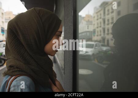 Femme dans hijab regardant par une fenêtre de magasin Banque D'Images