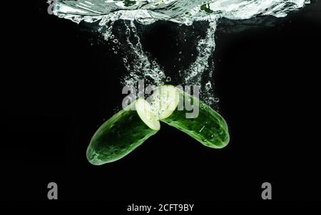 Concombre coupé dans la moitié de l'eau éclabousse isolé sur fond noir. Une alimentation saine. Banque D'Images
