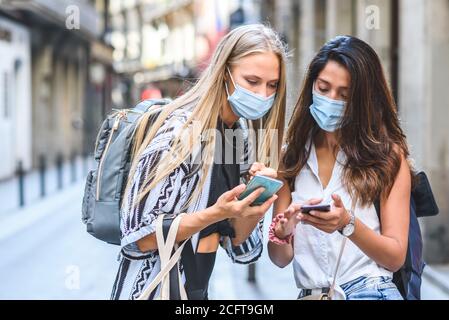 deux jeunes femmes touristes portant des masques et des sacs à dos sont vérification des téléphones mobiles dans les rues d'une ville Banque D'Images