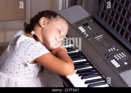 enfant fille en robe blanche dort sur les clés d'un piano électronique, synthétiseur Banque D'Images